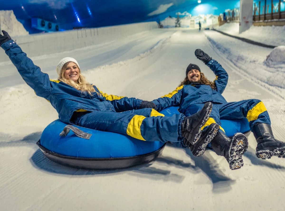 Casal curtindo a neve no Snowland em Gramado Casal sorridente na neve do Snowland em Gramado, usando roupas de frio e rodeado por cenário nevado